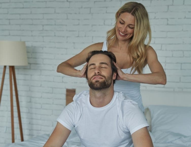 Une personne masse la tête de son conjoint, assis et détendu, lors d'un atelier en duo